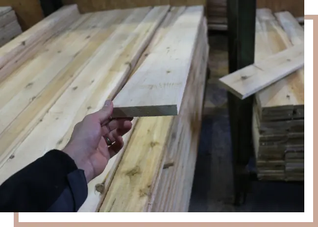 handing holding up a piece of lumber on top of a stack of lumber